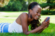Teenage black girl using a phone, lying on the grass