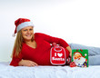 schwangere Frau liegend mit weihnachtsmütze hält weihnachtskugel
