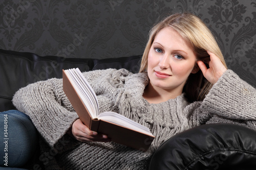 Photo: Smiling blonde woman relaxing reading book at home Smiling blonde woman relaxing reading book at home