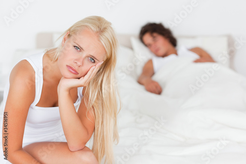 Foto : Unhappy woman sitting on a bed while her fiance is sleeping Unhappy woman sitting on a bed while her fiance is sleeping