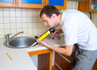 Plumber putting a silicone sealant to installing a kitchen sink