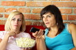 Two happy female friends eating popcorn and watching tv