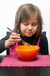 Young girl indoors eating soup from orange bowl
