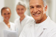 Closeup of happy old doctor with female colleagues at the back