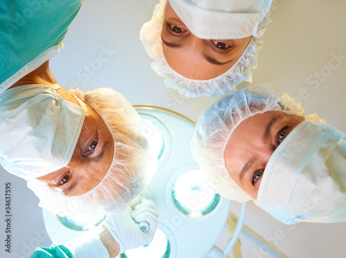 Foto: Surgeons looking down at patient in operation room Surgeons looking down at patient in operation room