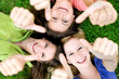 Three young girls lying down showing thumbs up sign Three young girls lying down showing thumbs up sign