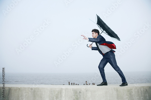 Photo: Businessman with an umbrella, wind blowing his umbrella away Businessman with an umbrella, wind blowing his umbrella away