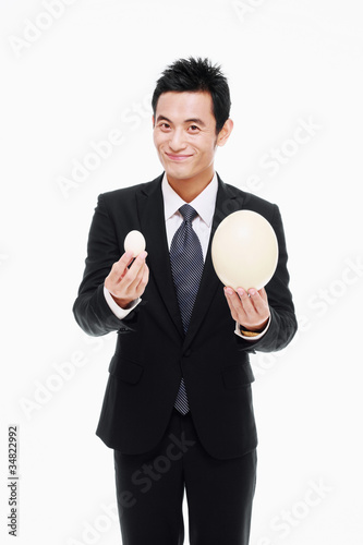 Photo: Businessman holding a big and a small egg Businessman holding a big and a small egg