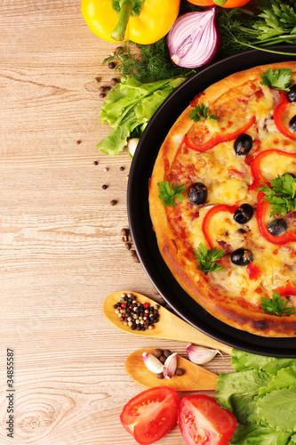 Photo: tasty pizza on the plate and vegetables on a wooden background tasty pizza on the plate and vegetables on a wooden background
