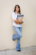 Pretty female student standing against a wall with books in her