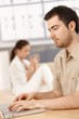 Young man using laptop at home woman in background