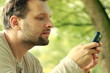 Happy young man sending sms, texting in the park