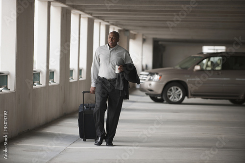 Photo: African businessman walking in parking garage with luggage African businessman walking in parking garage with luggage