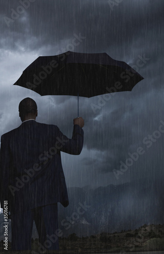 Photo: Black businessman holding umbrella in storm Black businessman holding umbrella in storm