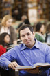 Mixed race man reading book in school library
