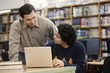Librarian helping student with laptop in school library