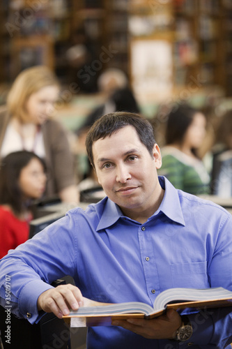 Photo: Mixed race man reading book in school library Mixed race man reading book in school library