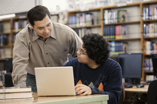 Photo: Librarian helping student with laptop in school library Librarian helping student with laptop in school library