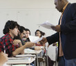 Teacher handing papers to students in classroom