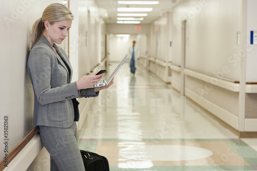 Photo: Caucasian businesswoman using laptop and cell phone in hospital hallway Caucasian businesswoman using laptop and cell phone in hospital hallway
