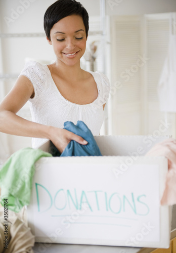 Photo: Mixed race woman putting clothing in donation box Mixed race woman putting clothing in donation box