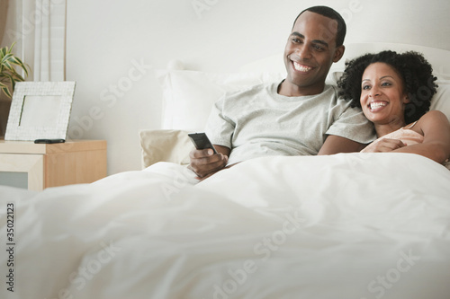 Photo: Couple laying in bed watching television Couple laying in bed watching television