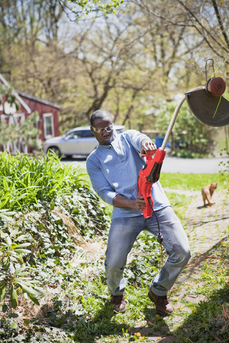 Foto: Black man struggling with weed trimmer Black man struggling with weed trimmer