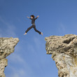 Mixed race businesswoman jumping over gap between cliffs