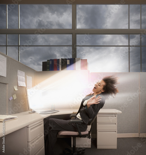 Photo: Light bursting from computer at mixed race businesswoman Light bursting from computer at mixed race businesswoman