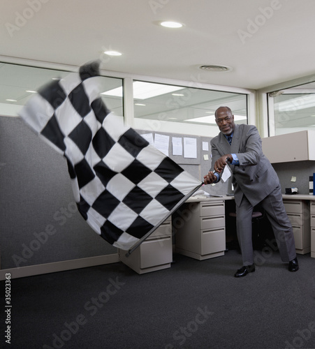 Photo: African American businessman waving checkered flag in office African American businessman waving checkered flag in office