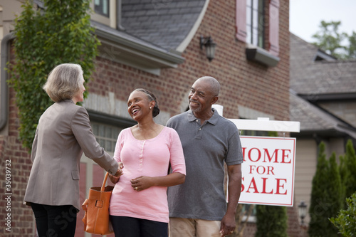 Foto: Realtor shaking hands with smiling couple outside house for sale Realtor shaking hands with smiling couple outside house for sale