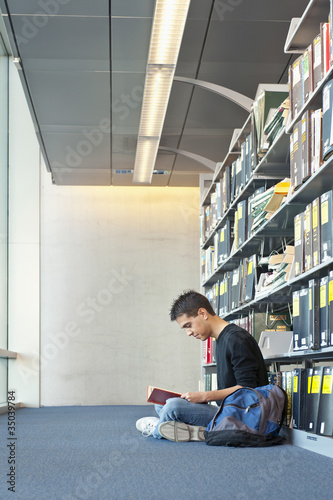 Photo: Hispanic student reading book on library floor Hispanic student reading book on library floor