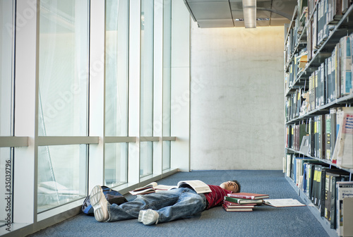 Foto: Books surrounding exhausted Hispanic student laying on library floor Books surrounding exhausted Hispanic student laying on library floor