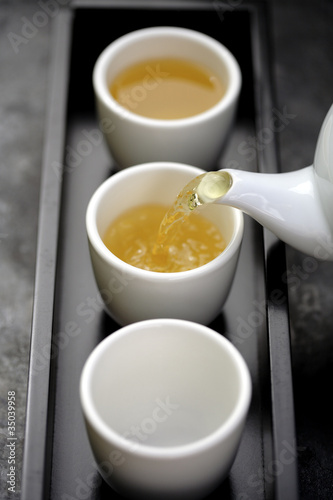 Photo: Green tea being poured from teapot into cups on tray Green tea being poured from teapot into cups on tray