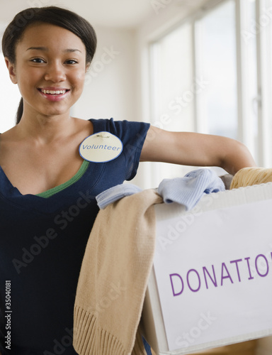 Photo: Smiling mixed race teenage girl wearing 'Volunteer' pin and holding box of donations Smiling mixed race teenage girl wearing 'Volunteer' pin and holding box of donations