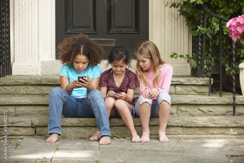 Photo: Girls text messaging with cell phones on front stoop Girls text messaging with cell phones on front stoop