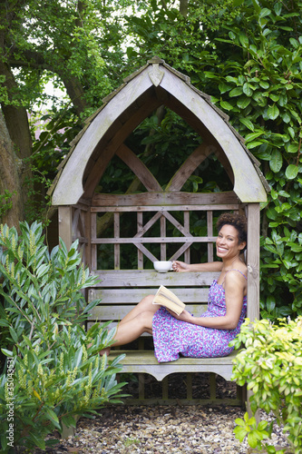 Photo: Mixed race woman reading book in backyard Mixed race woman reading book in backyard