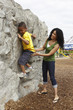 Black mother helping son climb rock wall