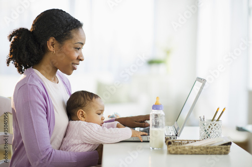 Photo: Mixed race woman holding baby and using laptop Mixed race woman holding baby and using laptop