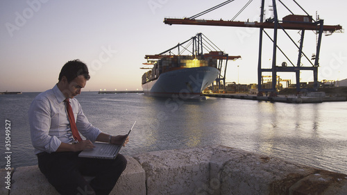 Foto: Hispanic businessman with laptop with container ship in background Hispanic businessman with laptop with container ship in background
