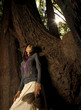 Woman standing on roots of large tree holding feathers