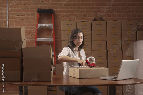 Photo: Hispanic woman taping cardboard box Hispanic woman taping cardboard box