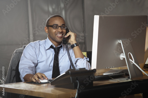 Photo: African American businessman working at desk and talking on telephone African American businessman working at desk and talking on telephone
