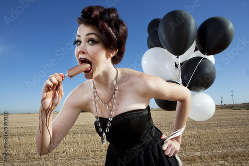 Photo: Glamorous woman holding balloons and eating popsicle Glamorous woman holding balloons and eating popsicle