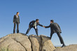 Businessman helping co-worker onto rock