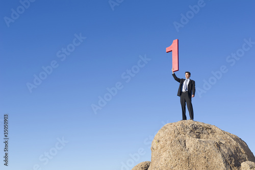 Photo: Caucasian businessman on rock lifting large number 1 Caucasian businessman on rock lifting large number 1