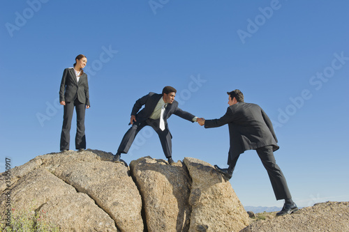 Photo: Businessman helping co-worker onto rock Businessman helping co-worker onto rock