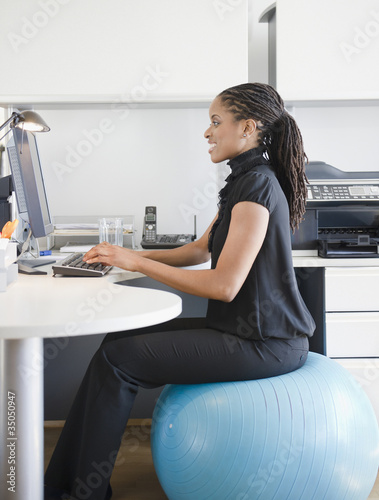 Photo: African American woman sitting on exercise ball at desk African American woman sitting on exercise ball at desk