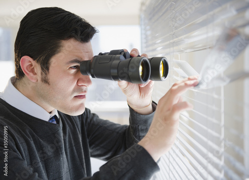 Photo: Hispanic businessman peering through window with binoculars Hispanic businessman peering through window with binoculars