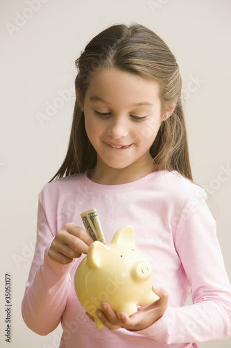 Foto: Caucasian girl putting money into piggy bank Caucasian girl putting money into piggy bank